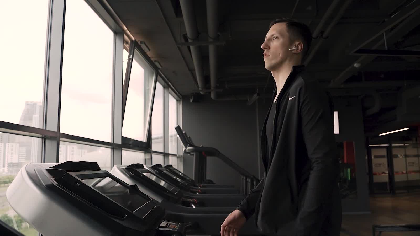 A runner using a treadmill beside tall gym windows
